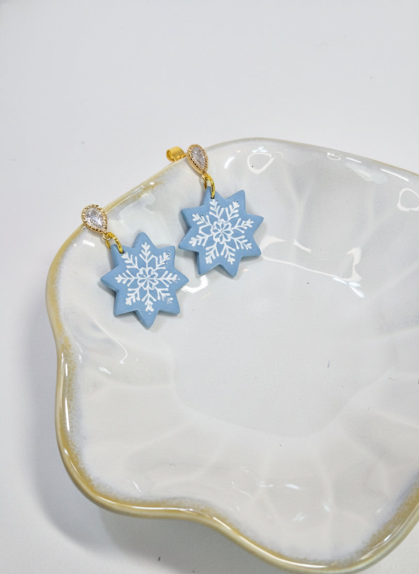 Blue snowflake earrings on a white dish with a gold rim